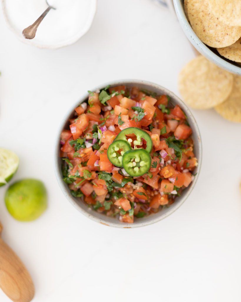 homemade pico de gallo salsa in a bowl with tortilla chips and jalapenos