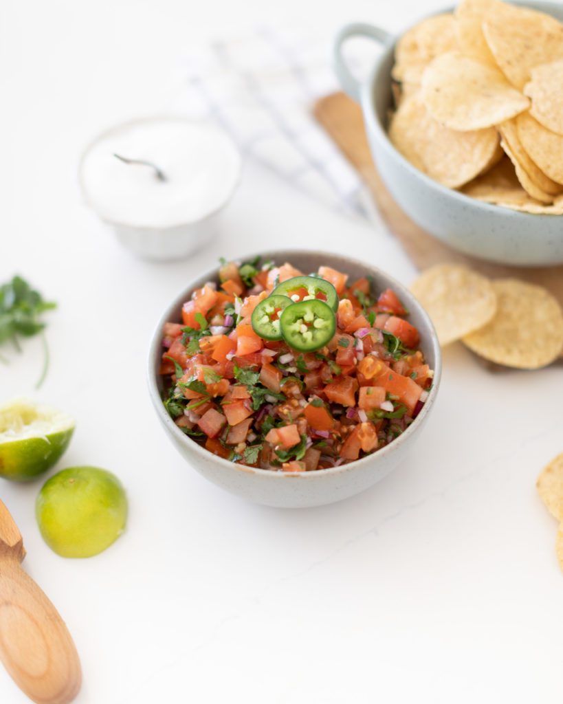 homemade pico de gallo salsa in a bowl with tortilla chips and jalapenos