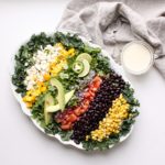 gluten free Mexican kale salad plated with colourful ingredients in rows on a white plate and table