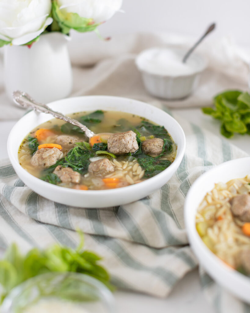 a bowl of Turkey Pesto Meatball Soup with meatballs, spinach, carrots, orzo and a silver spoon