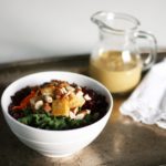 kale tofu glory bowl topped with almonds and dressing in a small glass pitcher