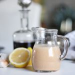 classic vinaigrette salad dressing in a glass pitcher with a lemon and vinegar bottle behind