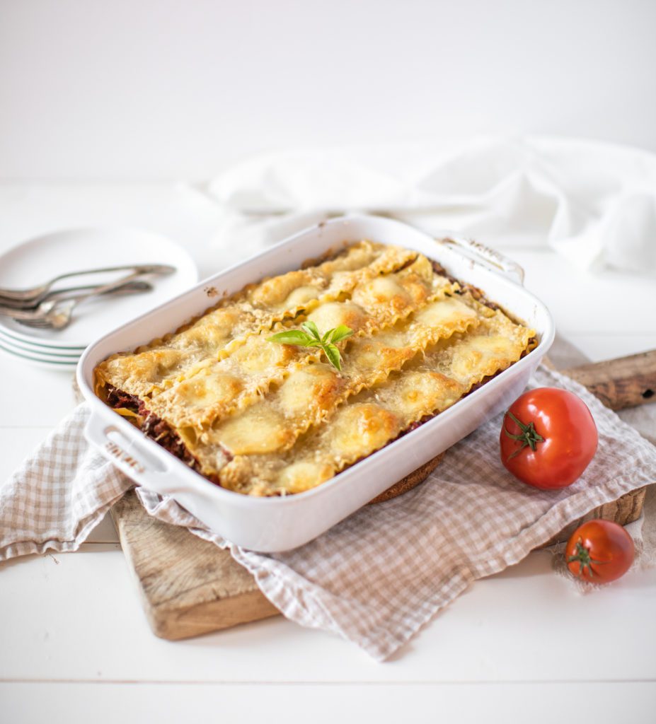 Rustic Italian Lasagne in a white baking dish with fresh tomatoes on the side