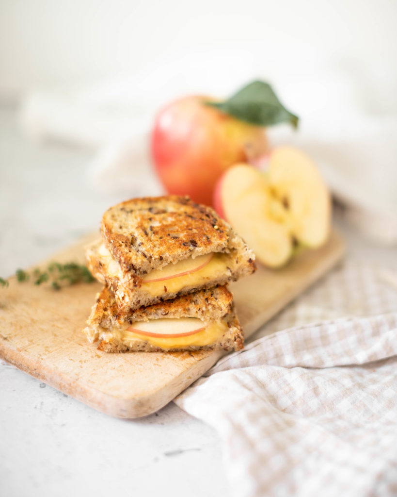 Gouda, Thyme & Apple Grilled Cheese cut in half with a fresh apple