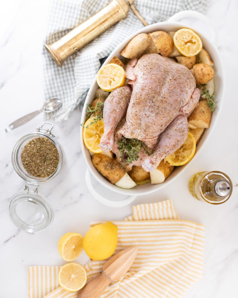 raw seasoned chicken in a baking dish with lemons and herbs