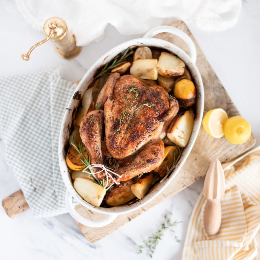 Greek Roasted Chicken & Potatoes in a baking dish with fresh lemons