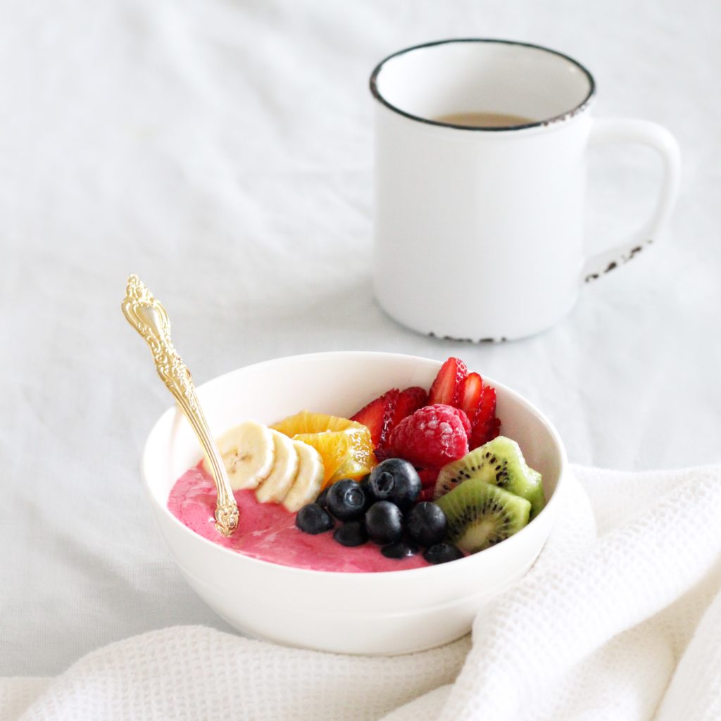 Raspberry Rainbow Smoothie Bowl in white bowl with white mug of coffee 