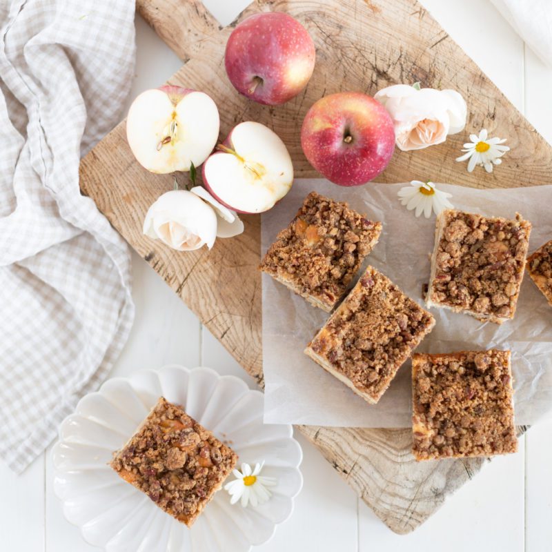 Apple Greek Yogurt Cake by Fraiche Living cut into squares on a wooden board with fresh apples