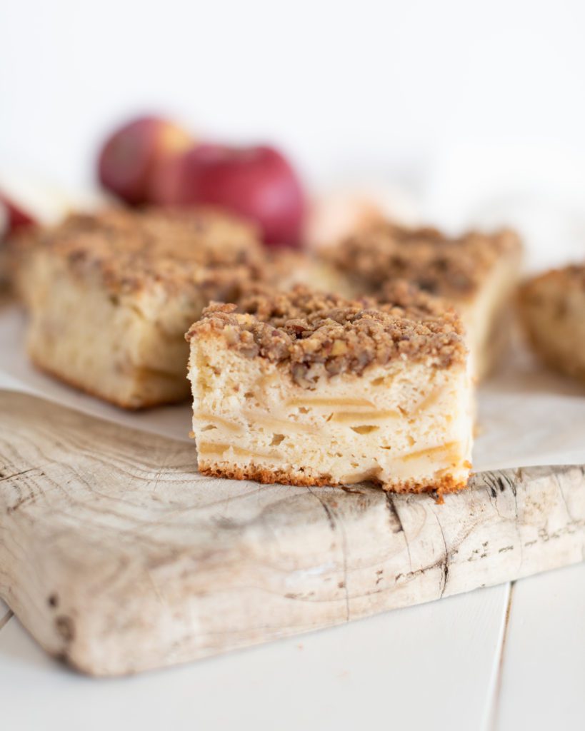 Slice of Apple Greek Yogurt Cake by Fraiche Living cut into squares on a wooden board with fresh apples