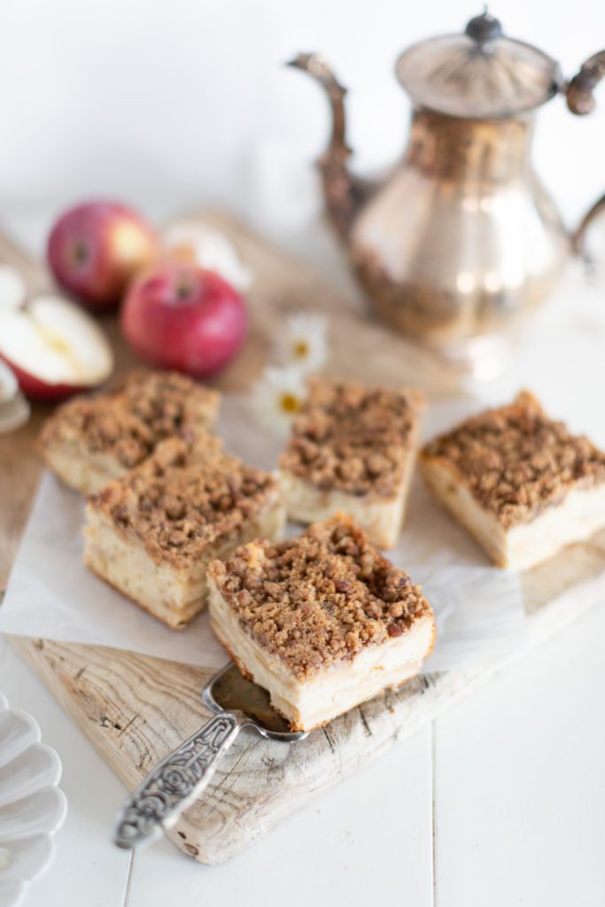 Apple Greek Yogurt Cake cut into squares on a wood board with fresh apples and a pot of tea