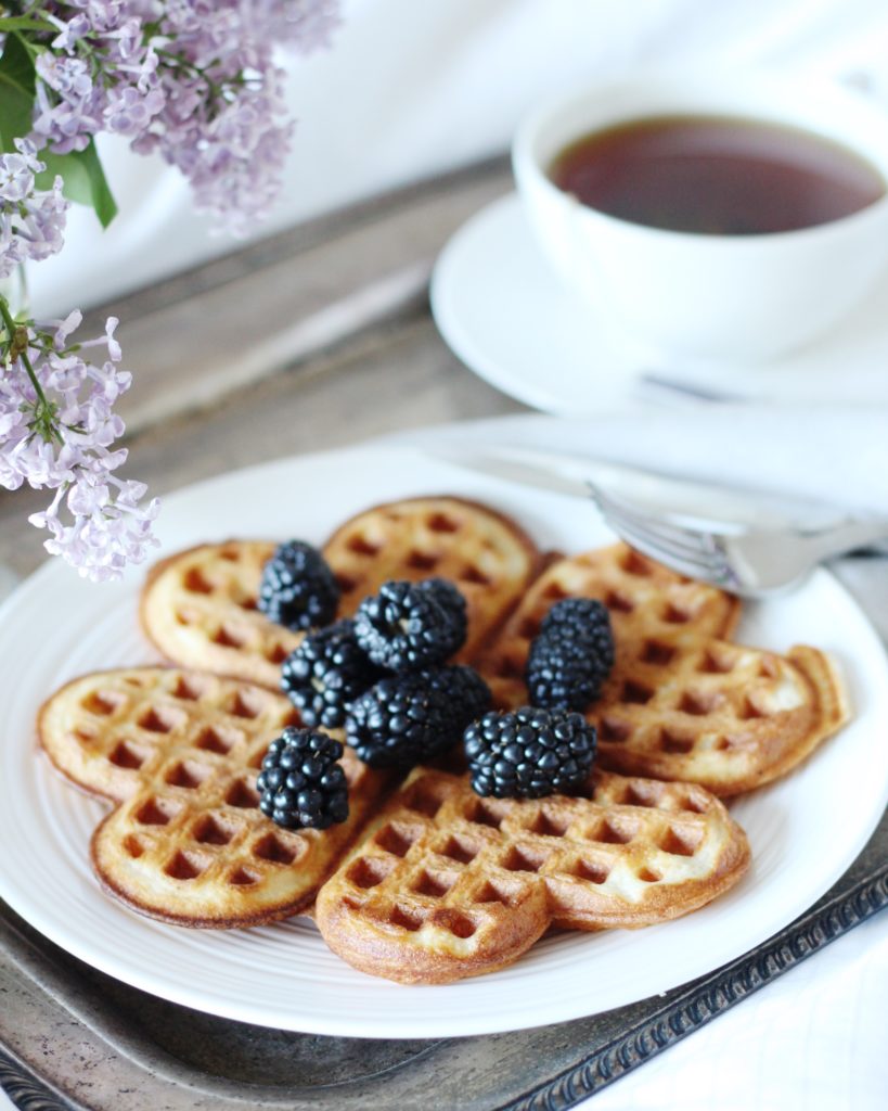 Vanilla Buttermilk Waffles topped with blackberries, cup of tea in white mug