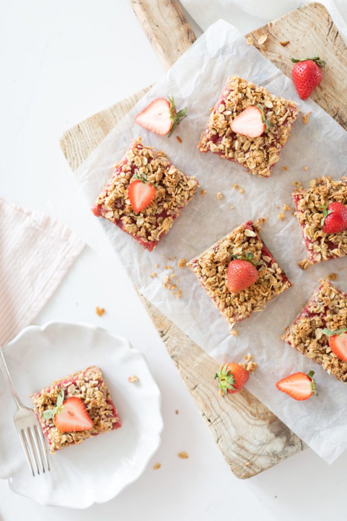 Strawberry Rhubarb Bars cut into squares on a white plate and wooden serving board