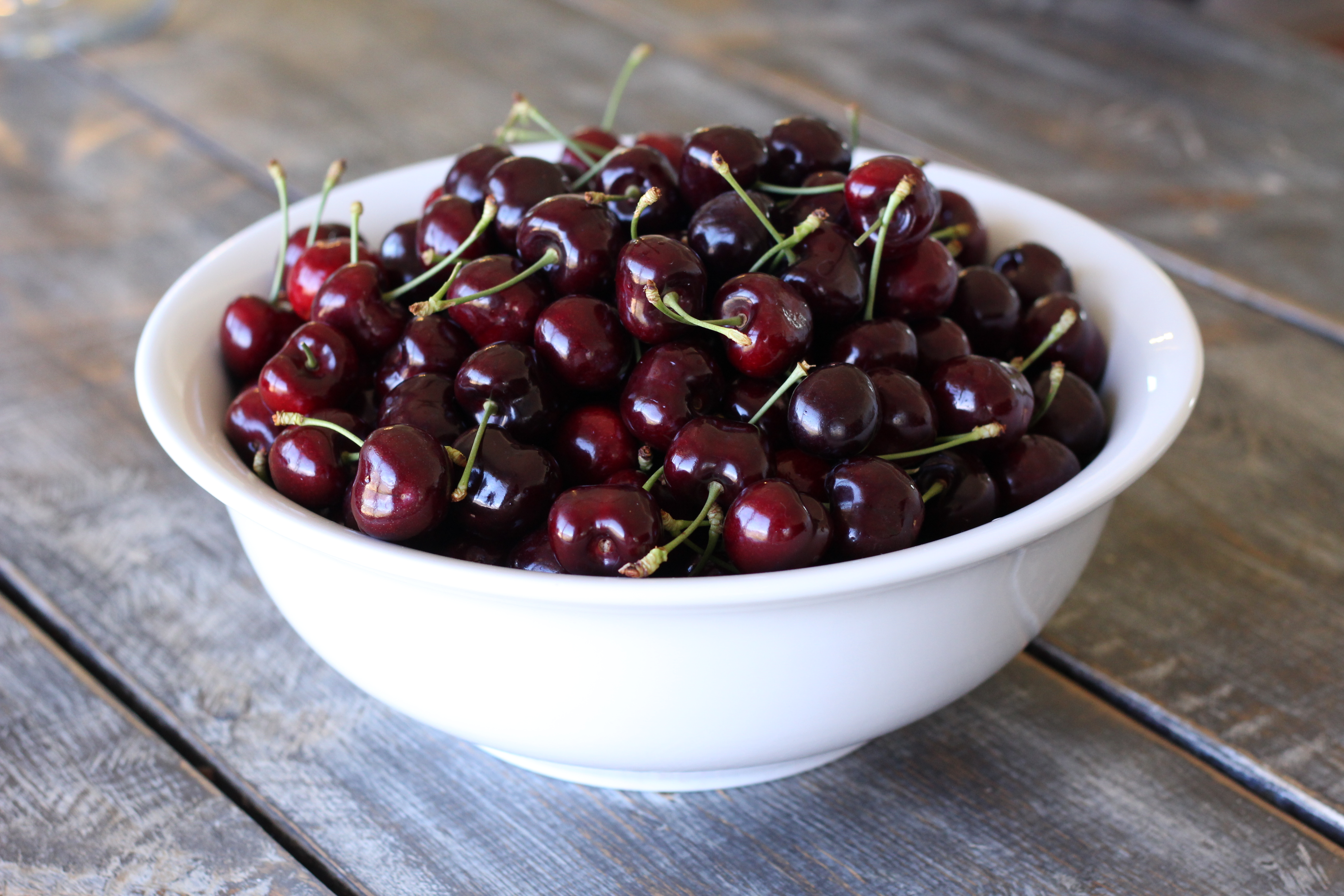 Fresh cherries in white bowl on wooden table 