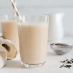 London Fog smoothie in a glass with a straw on a white surface, with another smoothie in the background