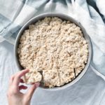hand reaching for vegan rice krispie squares in a bowl on a blue striped table cloth