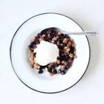 Berry Crisp in a white bowl with blueberries, oats, and topped with ice cream