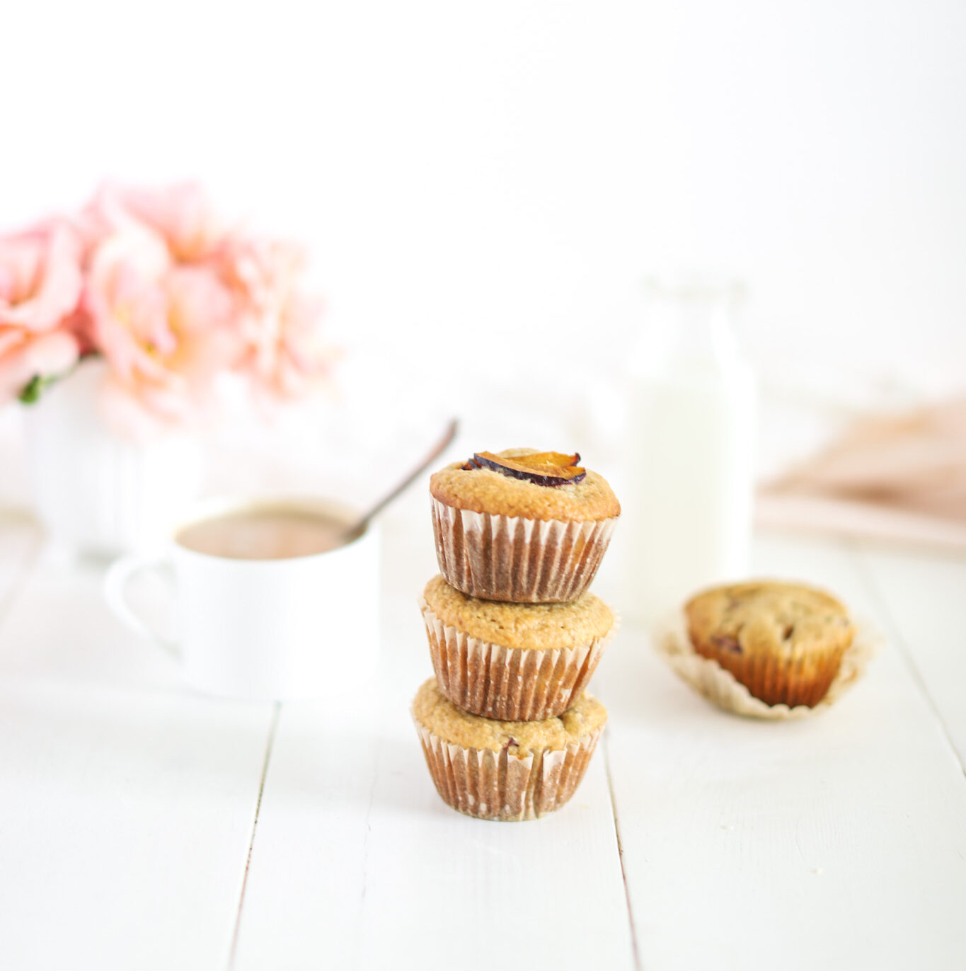 Plum Oat Bran Muffins stacked with cup of milk and flowers