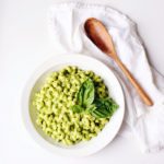 green goddess avocado pasta in a white bowl with a wooden spoon on a white surface