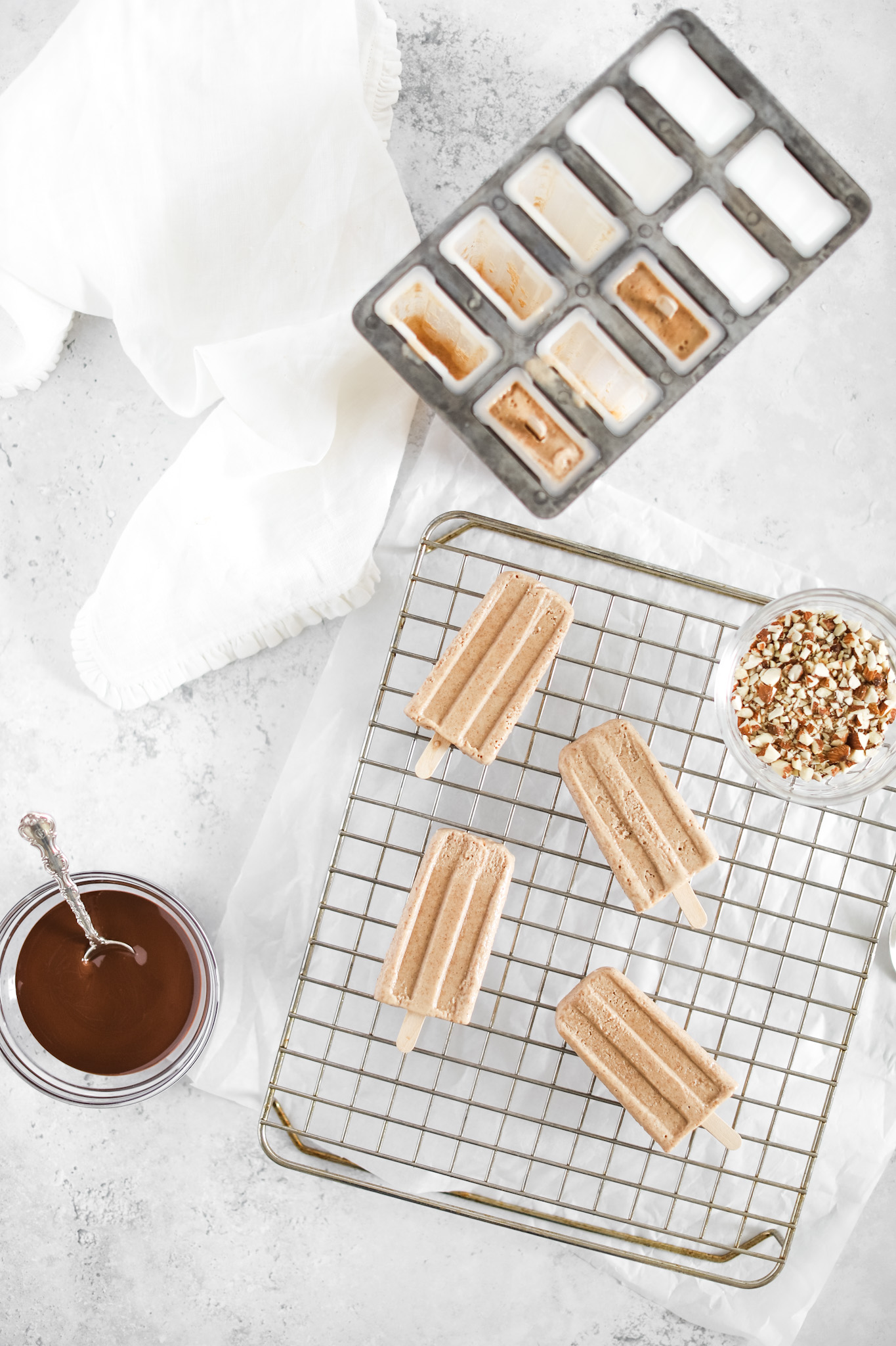 Almond Roca Popsicles by Fraiche Living on a wire rack with a bowl of melted chocolate and crushed almonds