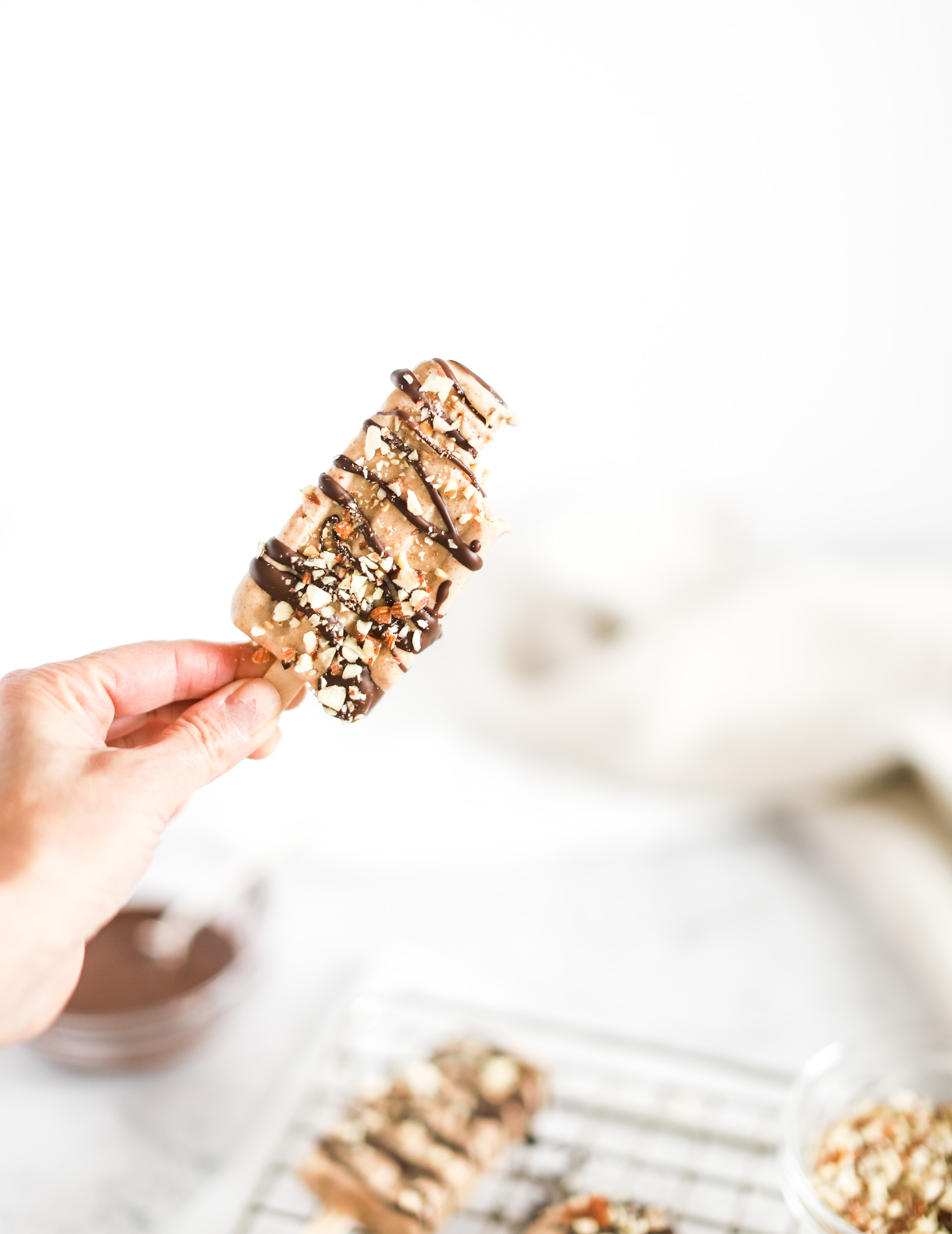 hand holding up an Almond Roca Popsicles by Fraiche Living covered with chocolate and nute