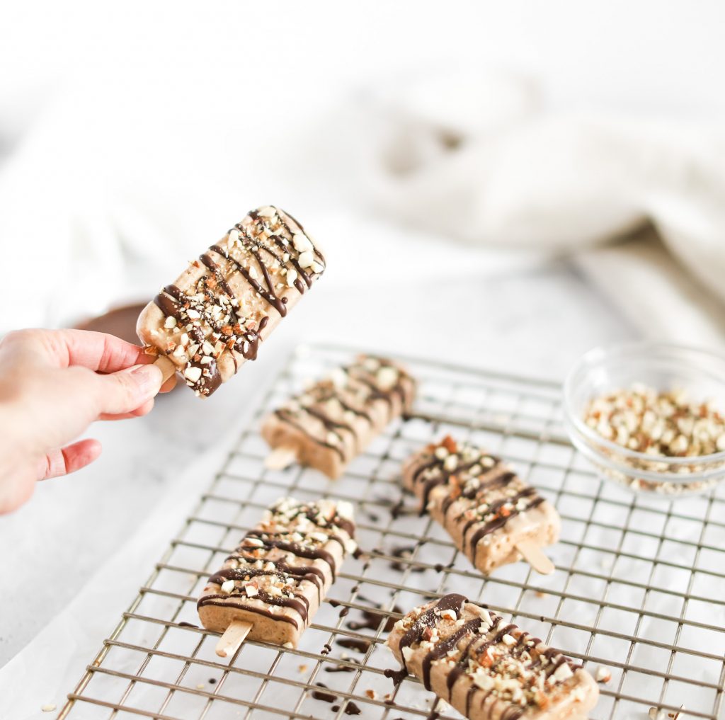 Fraiche Living Almond Roca Popsicles on a tray with a hand holding one up