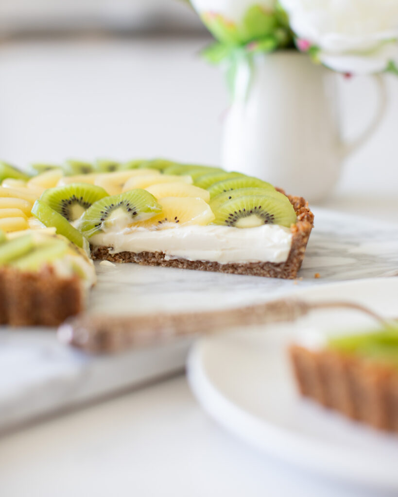 Kiwi Yogurt Tart by Tori Wesszer from Fraiche Living with a slice tek out of it, showing the layers of yellow and green kiwi fruit on top 