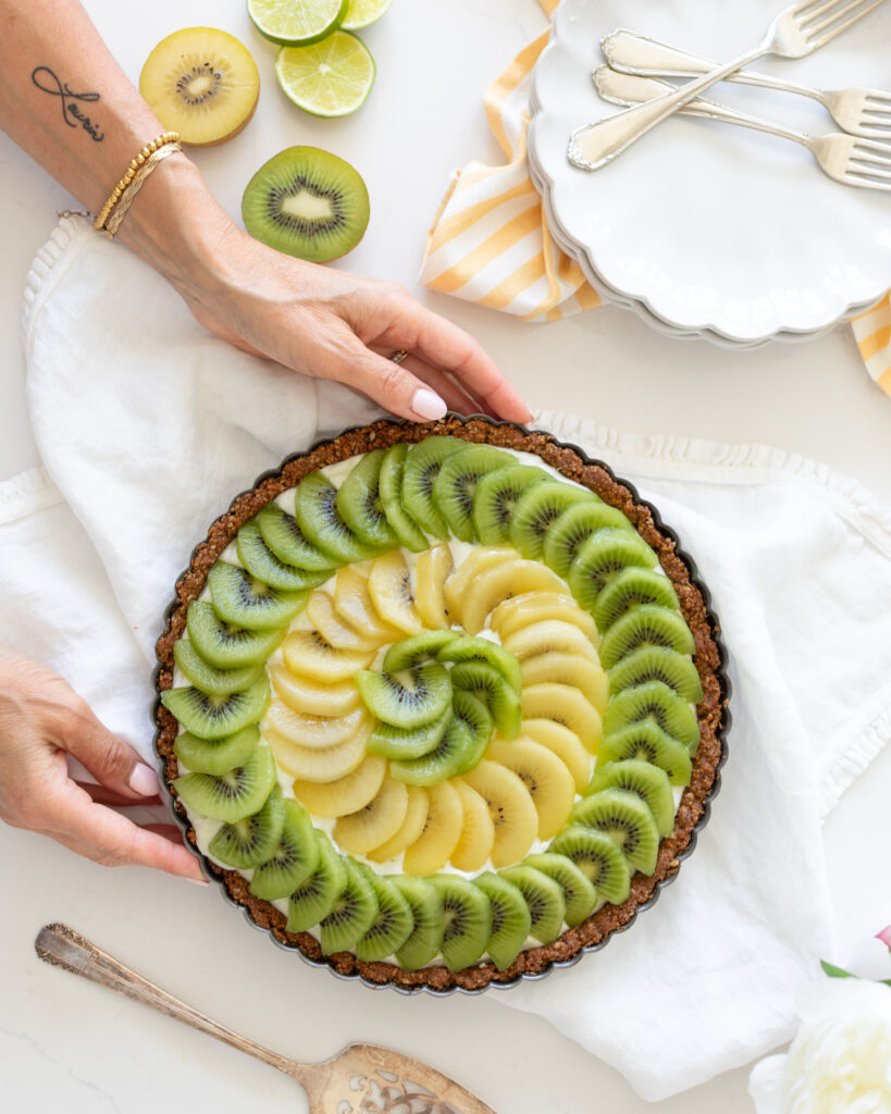 A hand holding the Kiwi Yogurt Tart by Tori Wesszer from Fraiche Living in a tart pan with layers of yellow and green kiwi fruit on top 