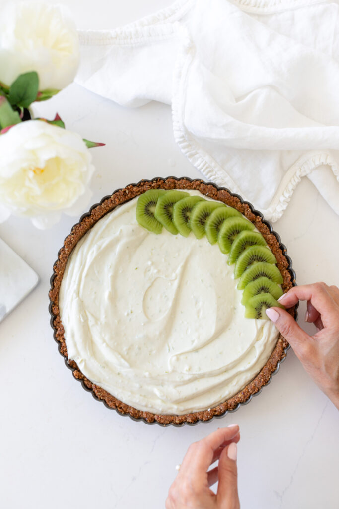 a hand layering green kiwi fruit slices on top of the yogurt filling for a Kiwi Yogurt Tart