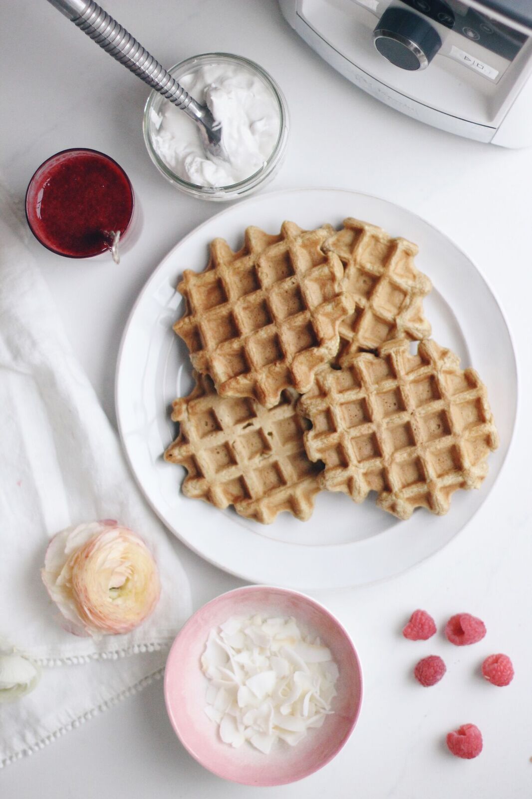 A plate of waffles stacked with raspberry sauce and coconut with the Vitamix blender.