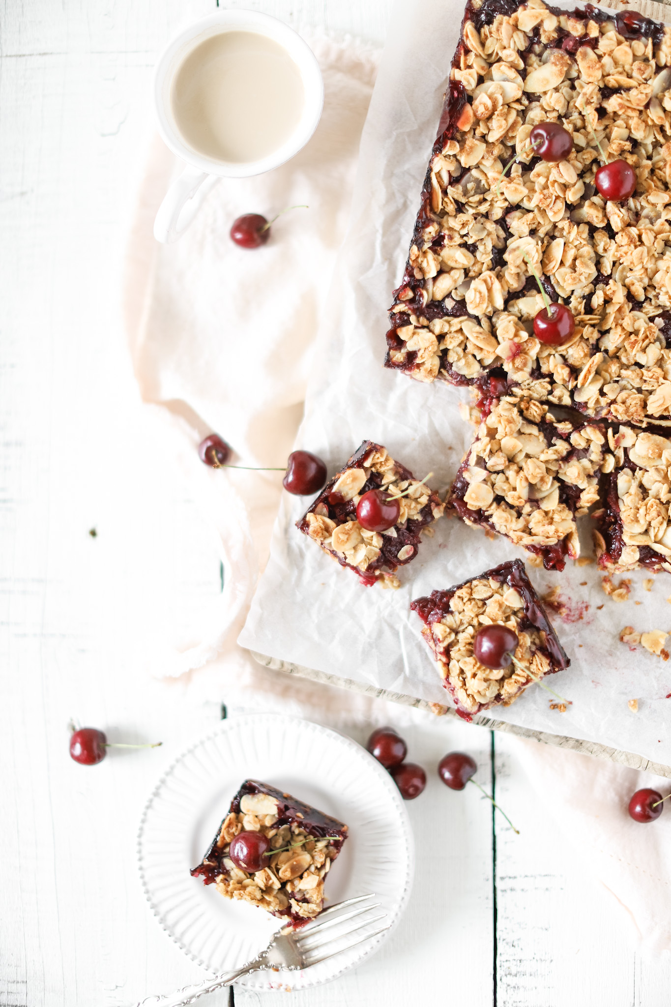 Okanagan Cherry Oat Bars cut into squares on a plate and wooden board and cherries