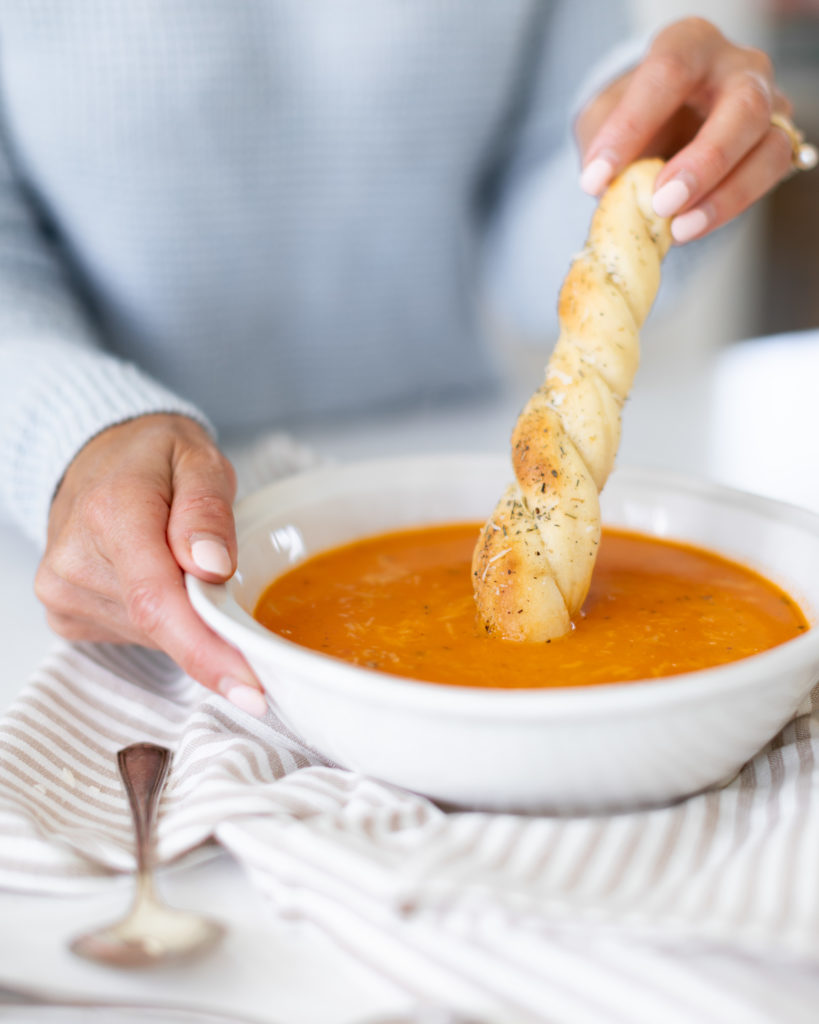 dipping a bread stick into a bowl of roasted tomato soup