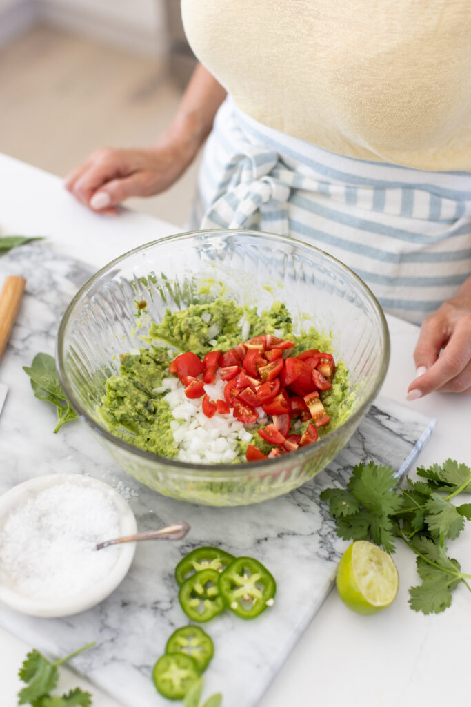 Bowl of creamy guacamole topped with diced tomatoes and onions.