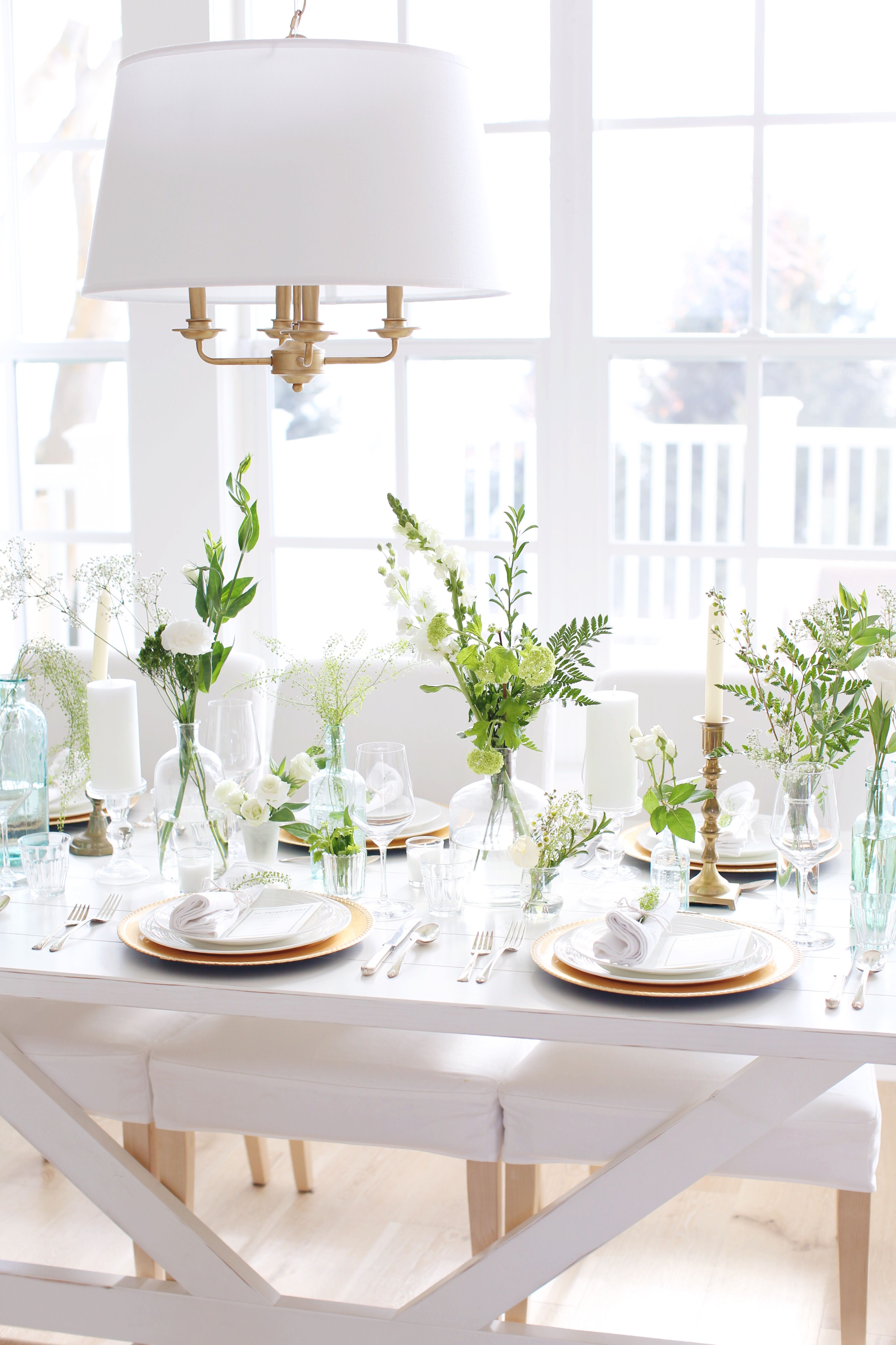 St. Patrick's Day Table Setting inspiration with gold chargers, greenery, green glass and white linens - that is also perfect for a light green and white wedding or dinner party.