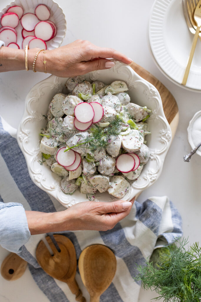 hands holding a bowl of creamy dill potato salad with baby potatoes, radish and fresh dill