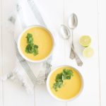 coconut pumpkin soup in two bowls on a white table, topped with cilantro