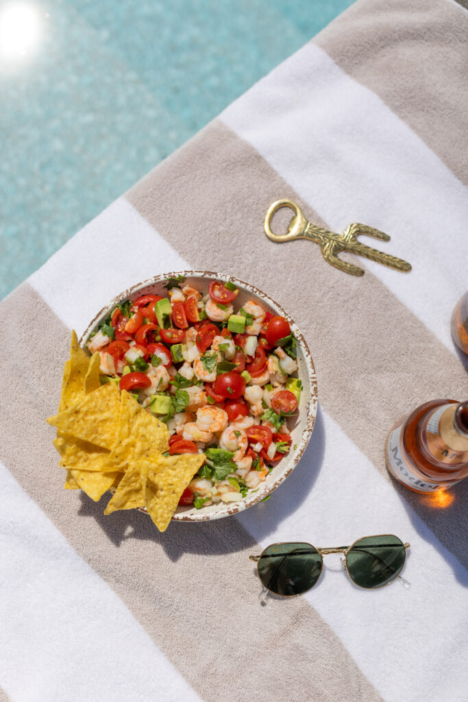 Bowl of Shrimp Avocado Salsa on pool towel next to pool, with tortilla chips on the side, garnished with lime and cilantro.