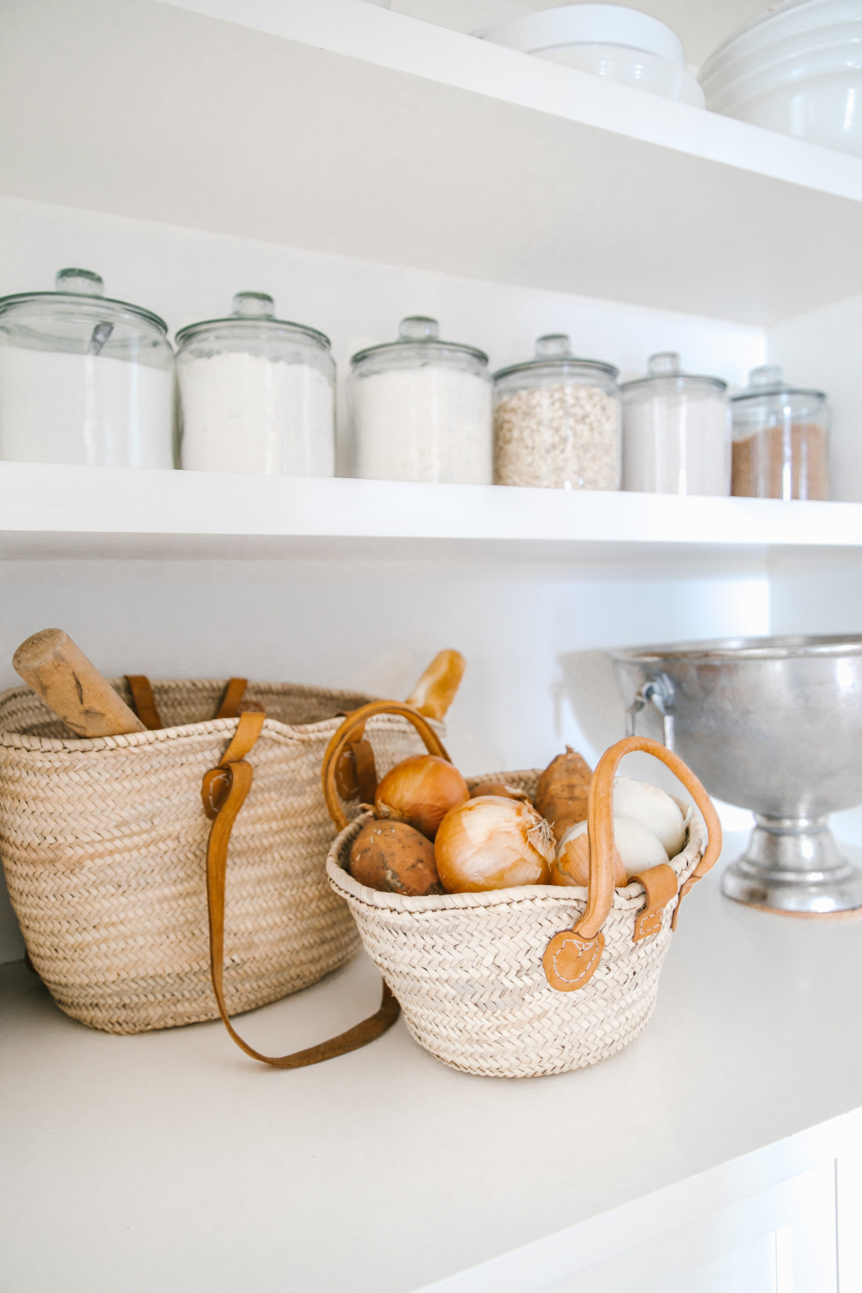 Our white butler's pantry reveal with an arched doorway, vintage chandelier lighting and open shelving with these white bowls, baskets and glass jars for storage!