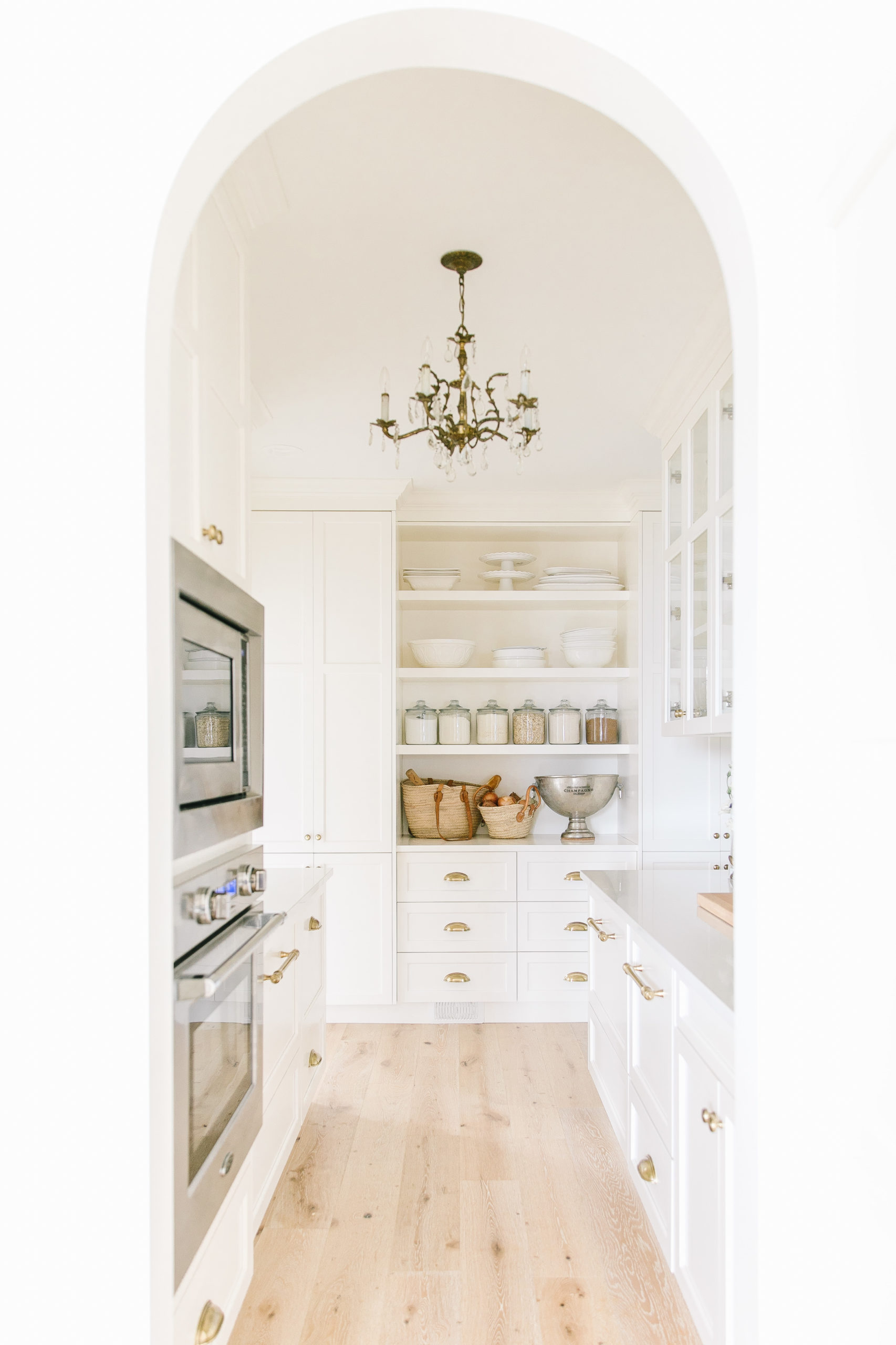 Our white butler's pantry reveal with an arched doorway, vintage chandelier lighting and open shelving. 