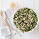 arugula quinoa salad in a white bowl with wooden utensils and dressing on the side