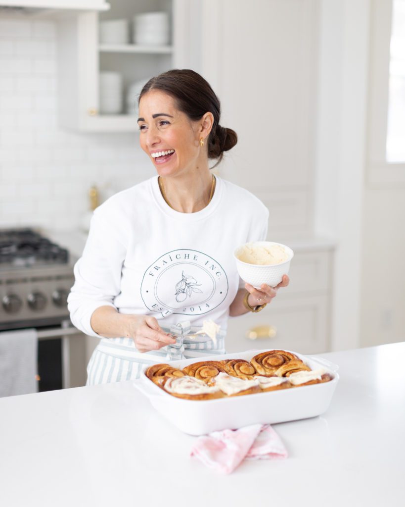 Woman smiling while icing homemade cinnamon buns