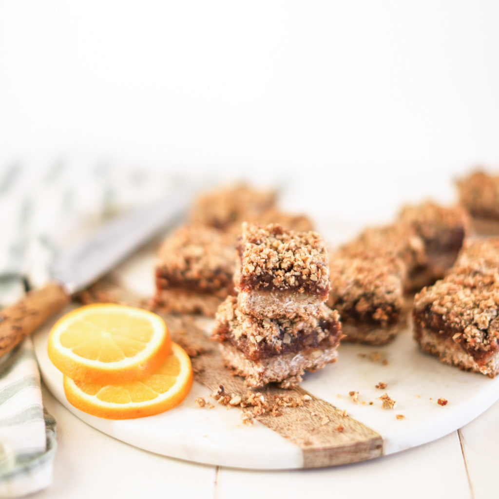 healthier date bars cut into squares and stacked on a tray with an orange slice