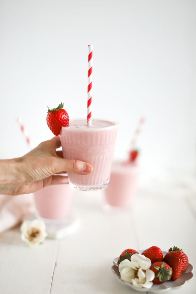 hand holding glass full of strawberry coconut milk drink