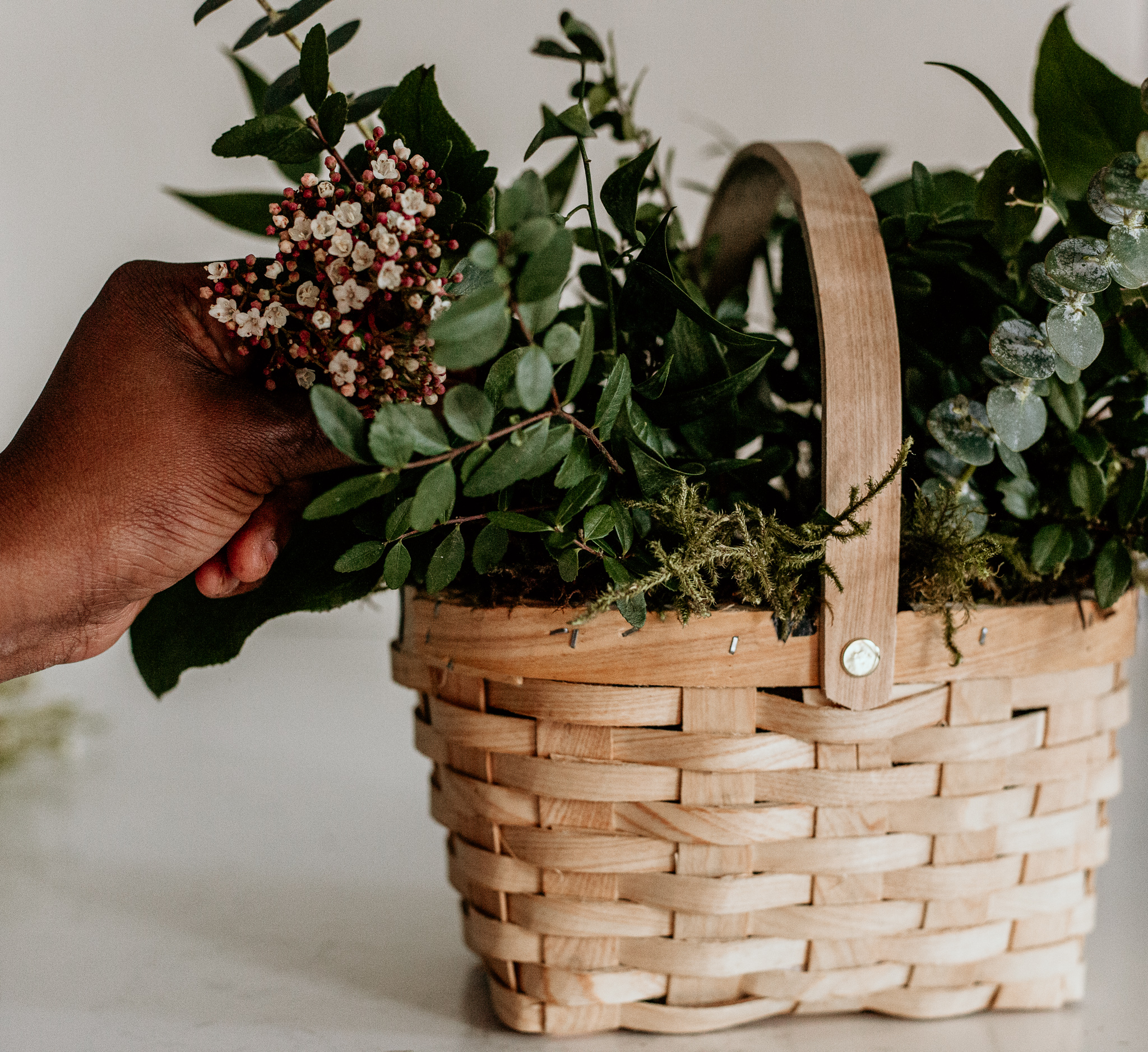 adding greenery to spring floral arrangement basket