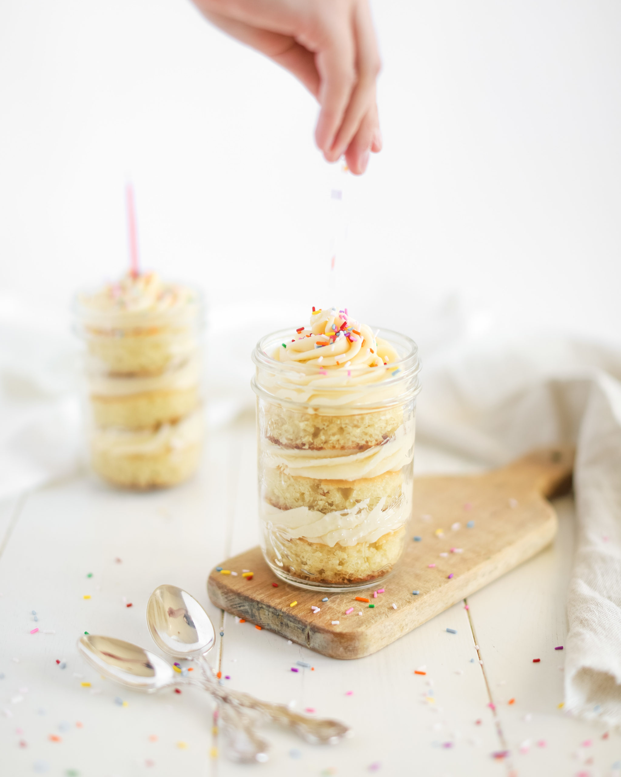 a hand topping a birthday cake in a jar with sprinkles