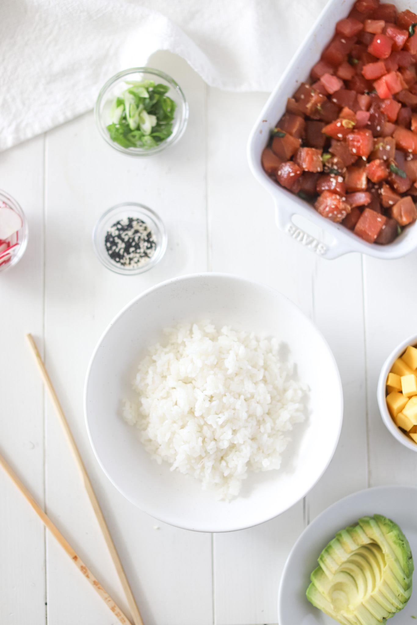 Bowls of Ingredients for Tuna Poke Bowls like : rice, tuna, avocado, mango, green onions