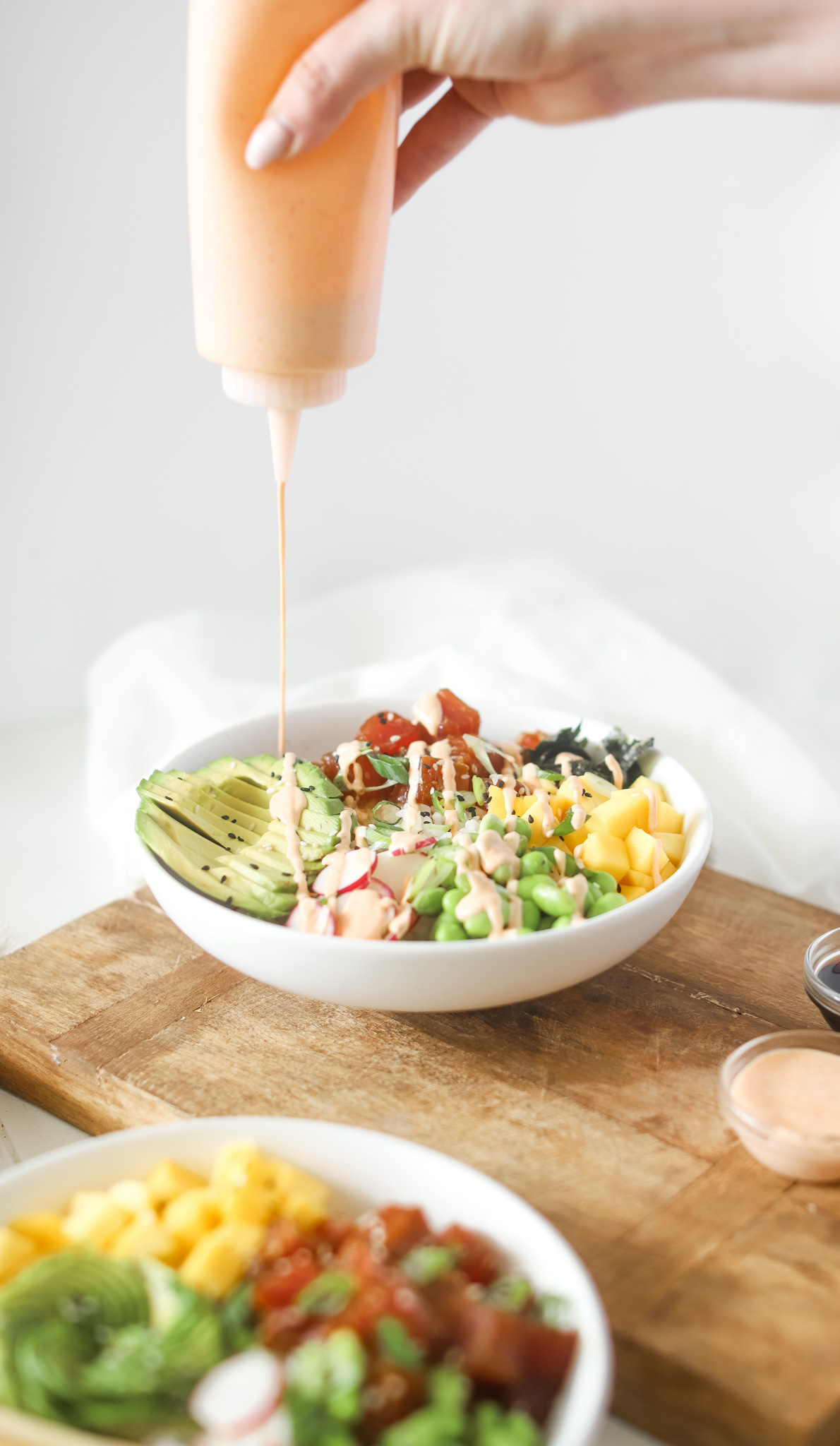 Bottle drizzling spicy mayo on to Tuna Poke Bowls