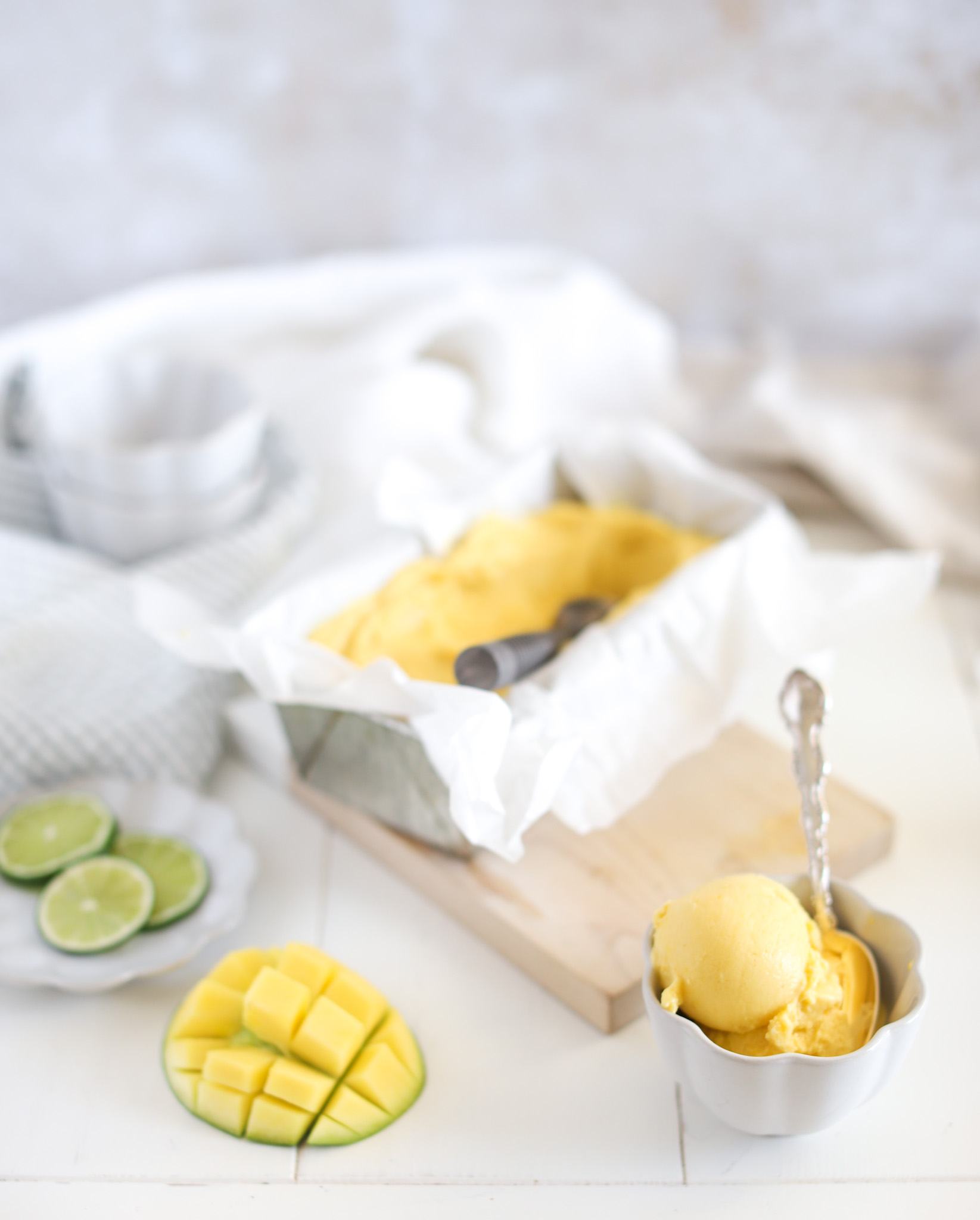 coconut mango nice cream dairy free fraiche living in loaf pan and bowls with spoon and fresh mango and lime
