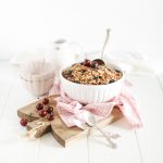 dark chocolate cherry granola fraiche living in white bowl with silver scoop and fresh cherries