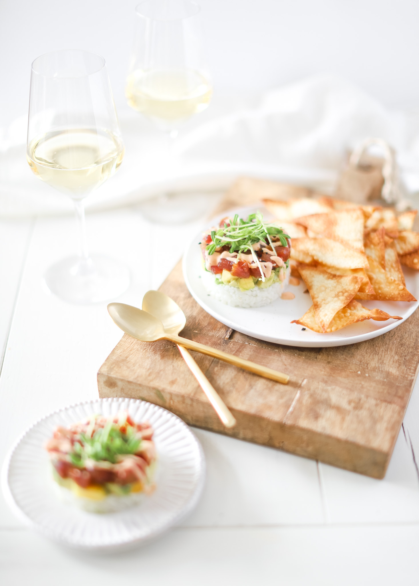tuna stack with wonton chips on plate with two spoons and glasses of wine