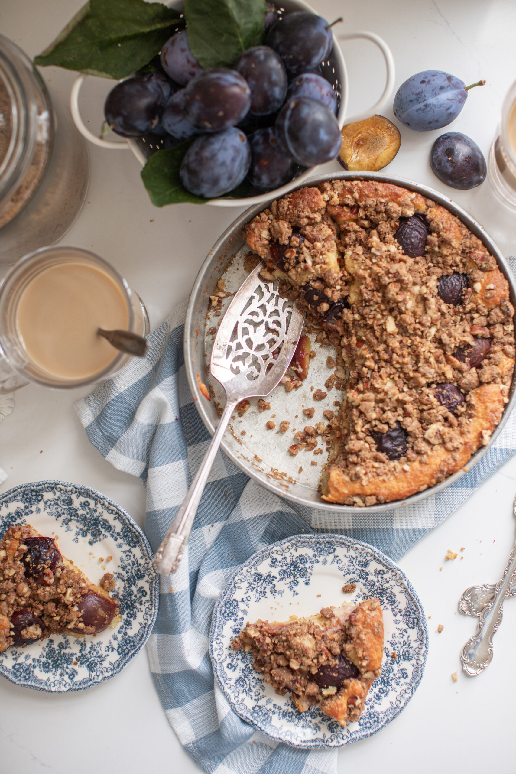Overhead shot of a whole plum coffee cake with streusel topping surrounded by fresh plums.